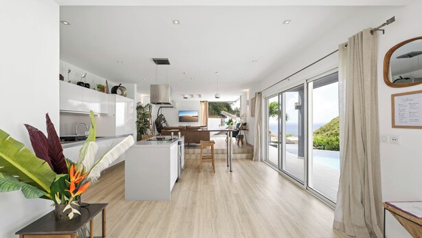 A modern kitchen with a central island, a dining area with a view, and a large sliding glass door to a balcony. - SUNSET VILLA ANGEL **** (saint barthelemy)
