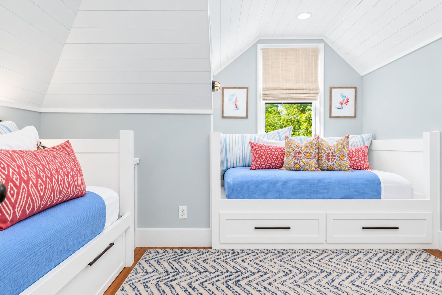 A bedroom with two beds, a window with a view of greenery, and a patterned rug.