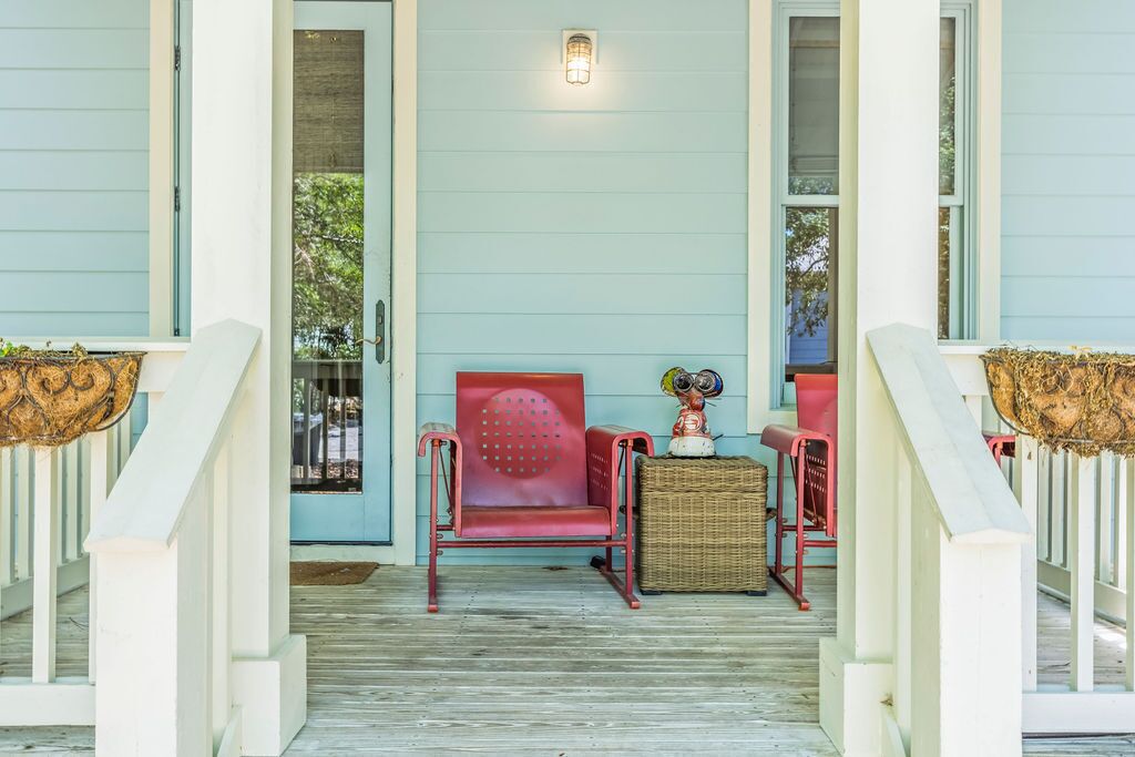 A porch with a red chair, a wicker table, and a small statue.