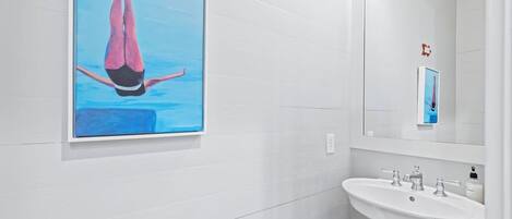 A bathroom with a large framed artwork of a diver, a white sink, and a mirror above it.
