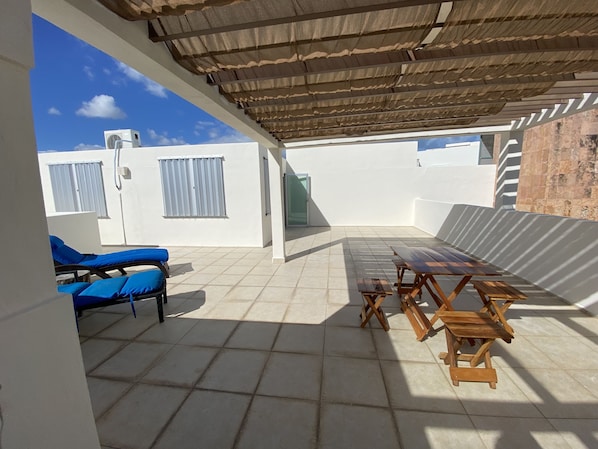 Relax in a shaded patio area with a tiled floor, wooden benches, and lounge chairs.