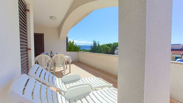 Un balcon avec des fauteuils de jardin blancs, une table avec une bouteille, et une vue sur un paysage montagneux.