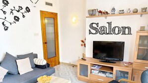 Uma sala de estar com sofá, mesa de centro, televisão e poltrona.