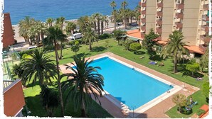 Vista de um apartamento com vista para uma piscina, palmeiras e um edifício com varandas.
