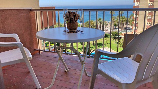 Varanda com mesa e cadeiras, com vista para o mar e edifícios.