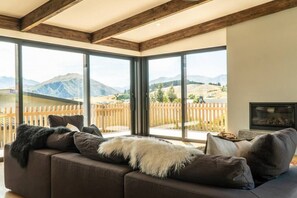 A modern living room with a large sectional sofa, a fireplace, and a scenic mountain view through floor-to-ceiling windows.