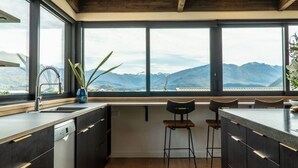 Une cuisine moderne avec des meubles de couleur sombre, un lave-vaisselle intégré et une grande fenêtre offrant une vue sur les montagnes.