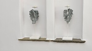 En hvid væg med to hvide hylder, der fremviser dekorative metalfigurer.