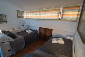 A bedroom with two single beds, a small bedside table, a nightstand, and a window with striped curtains.