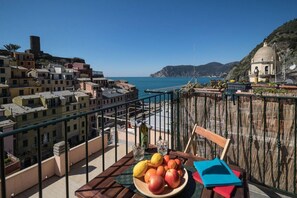 A balcony with a table, a plate of fruit, and a view of a coastal town.