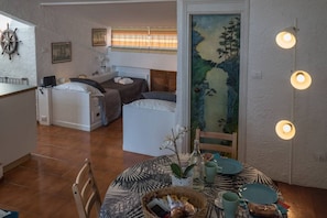 A compact living space with a kitchenette, a dining area with a round table, and a bedroom with a bed and a headboard.