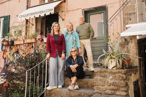 A group of people standing and sitting on a stone staircase outside a building with a sign reading 'CINQUETERIVIERA.COM'.
