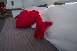 Un lit avec un doudou rouge et une literie blanche.