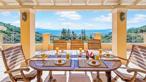 A covered outdoor dining area with a table set for breakfast, overlooking a scenic view of the sea and hills. - Villa Sivilla - Four Bedroom Villa, Sleeps 8 (Nisaki)