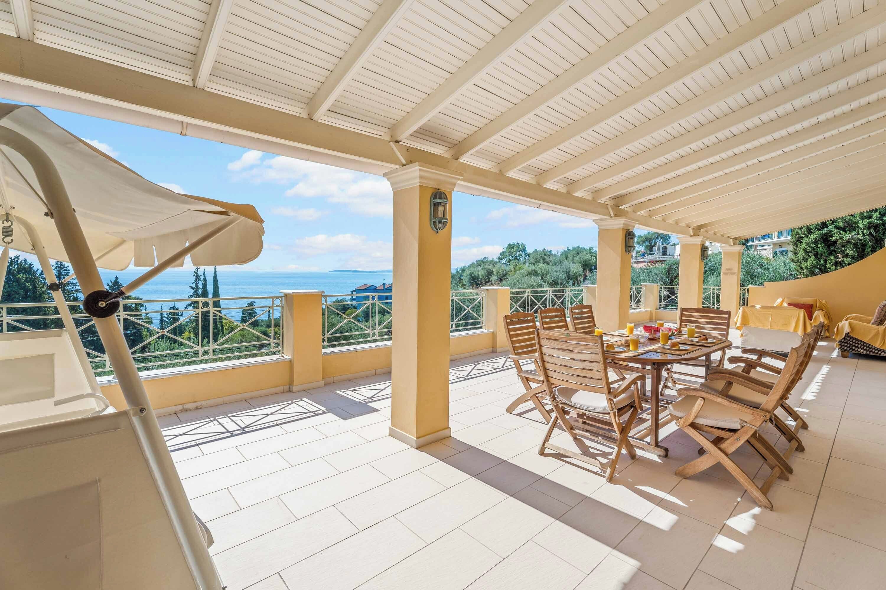 A covered patio with a table and chairs, a view of the sea, and a railing.