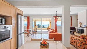 Eine moderne Küche mit Edelstahlgeräten, ein Essbereich mit Glastisch und ein Balkon mit orangenen Vorhängen.