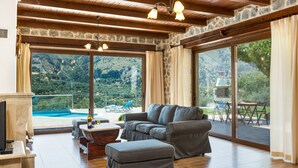 A spacious living area with a large gray sectional sofa, a wooden coffee table, and a stone fireplace. Large windows offer a view of a mountainous landscape.