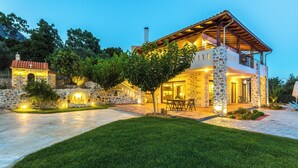 A two-story stone house with a balcony, a paved driveway, and a well-maintained lawn.