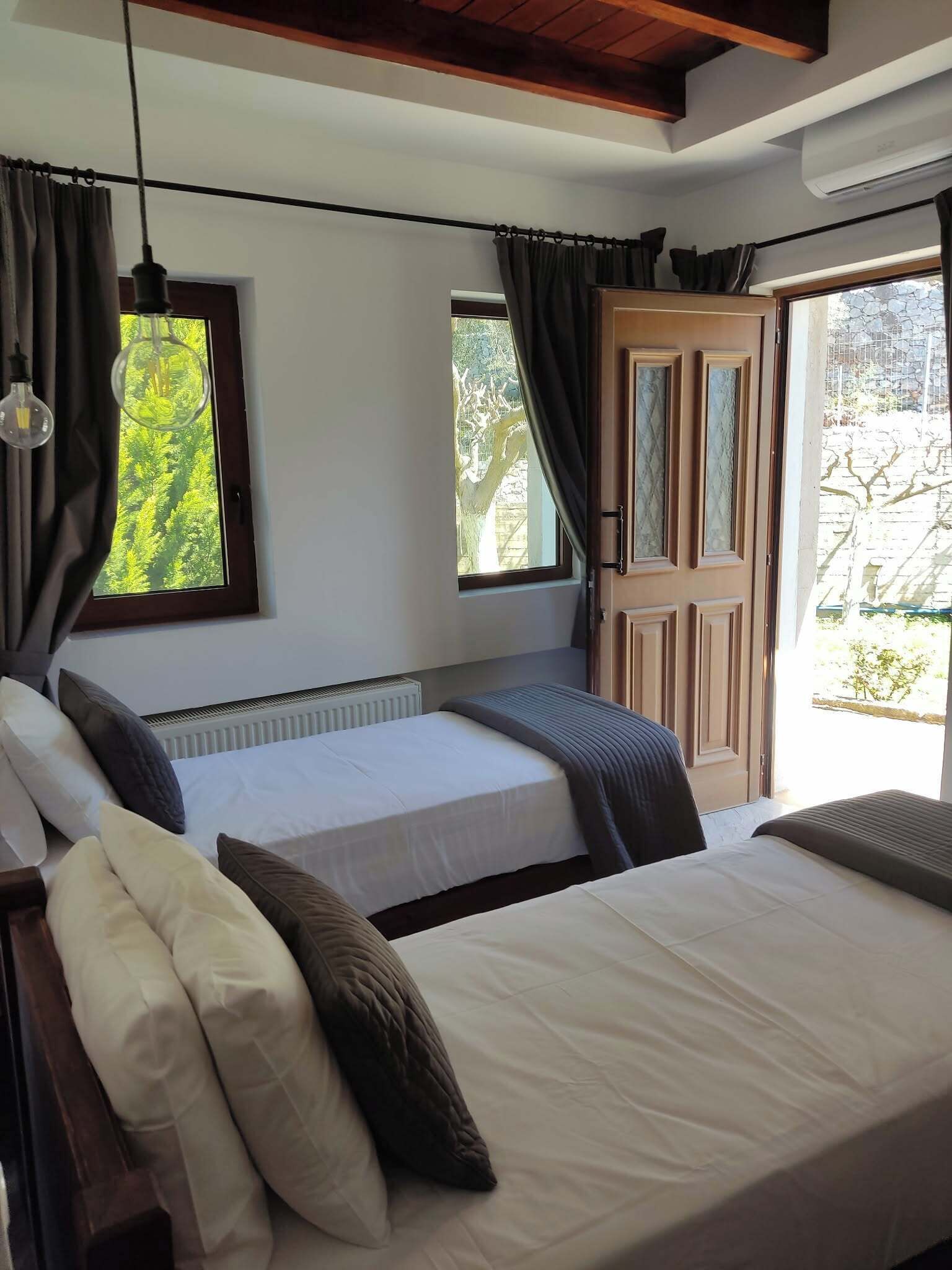 A bedroom with two beds, a window with curtains, a radiator, and a door leading to an outdoor area.