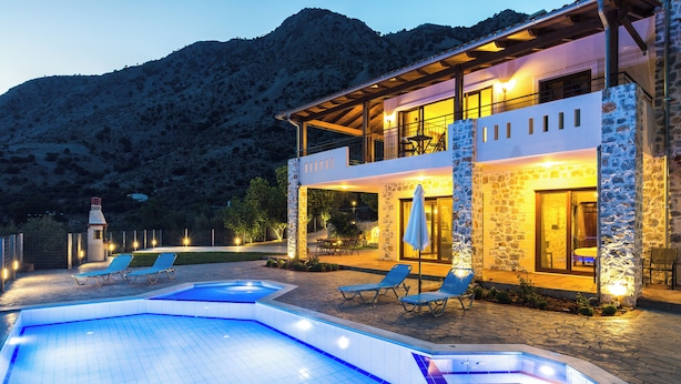 A two-story stone building with a swimming pool and lounge chairs.