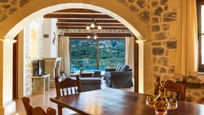 A stone-walled room with a wooden dining table, a sofa, and a television.