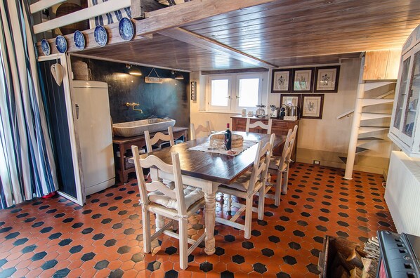Un comedor con una mesa y sillas de madera, una cocina con refrigerador y pileta, y un piso con diseño.