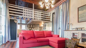 A red sectional sofa in a room with a high ceiling, a staircase, and a chandelier.