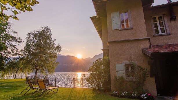 A house with a view of a lake and mountains at sunset.