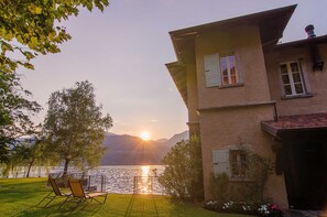 Una casa con vistas a un lago y montañas al atardecer.