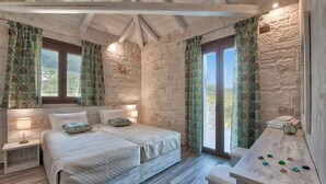 Quarto com parede de pedra, cama com cabeceira, mesa de cabeceira e vista para o exterior.