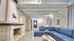 Uma sala de estar moderna com lareira de pedra, um sofá modular azul e uma mesa de centro de madeira com objetos decorativos.