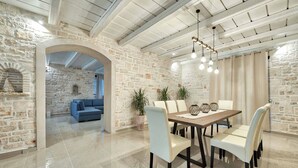 Uma sala de jantar com parede de pedra, sofá azul e mesa de madeira com cadeiras.