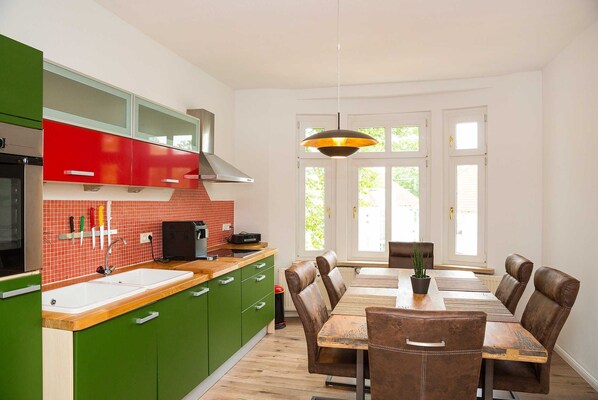 A modern kitchen with green cabinets, a double sink, and a dining area with a wooden table and leather chairs.