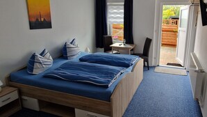 A bedroom with a bed, bedside tables, a desk, and a chair. There is a window with curtains, a door leading outside, and a small balcony area. - Double room 1 - Ankes Pension - Object 28383 (Rostock)