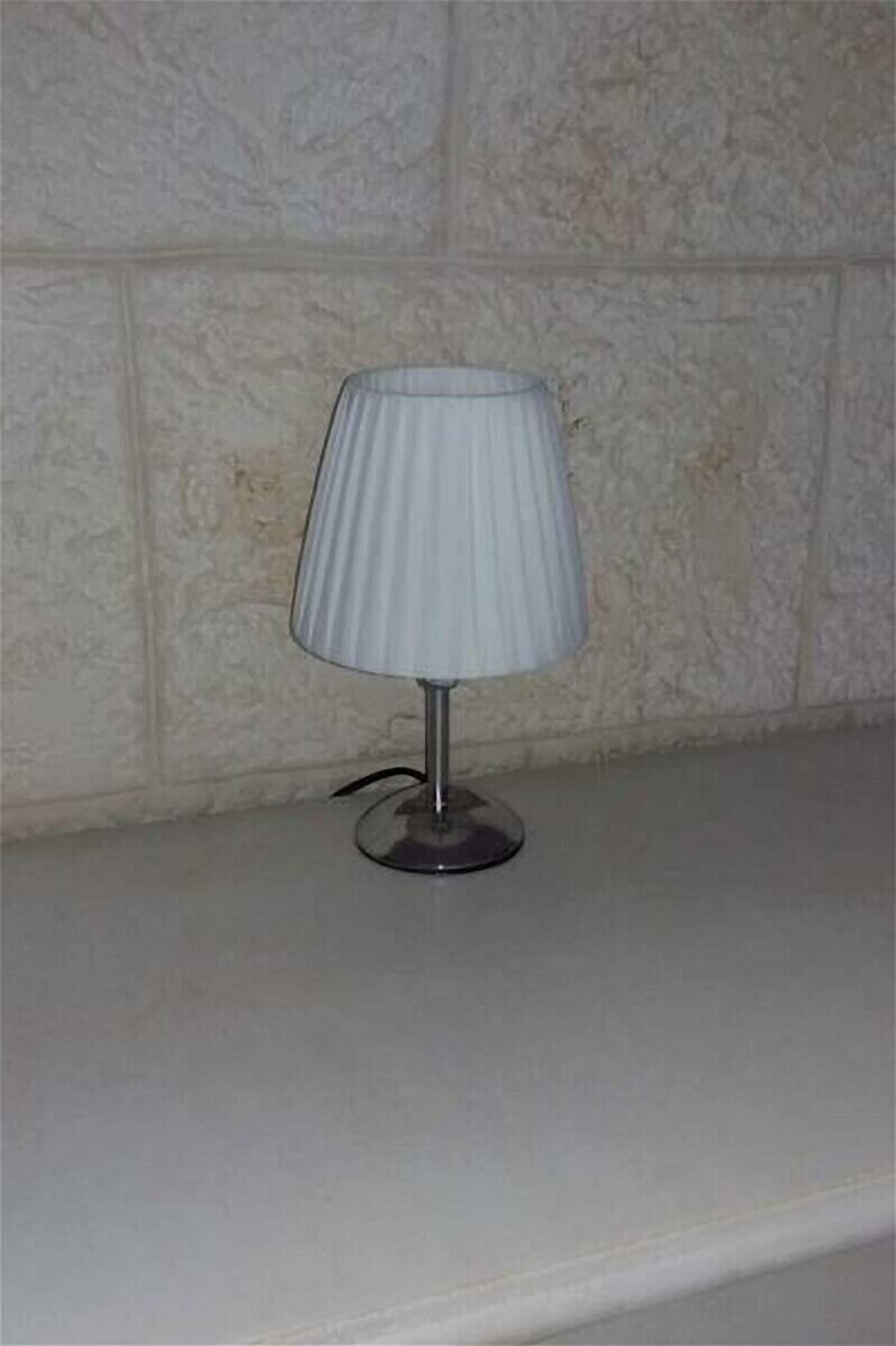 Una lampada da tavolo con paralume a coste su un tavolo bianco, con una parete dalla superficie irregolare.