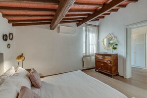 Een slaapkamer met een houten plafond, een bed met witte beddengoed, een dressoir, een spiegel en een radiator.