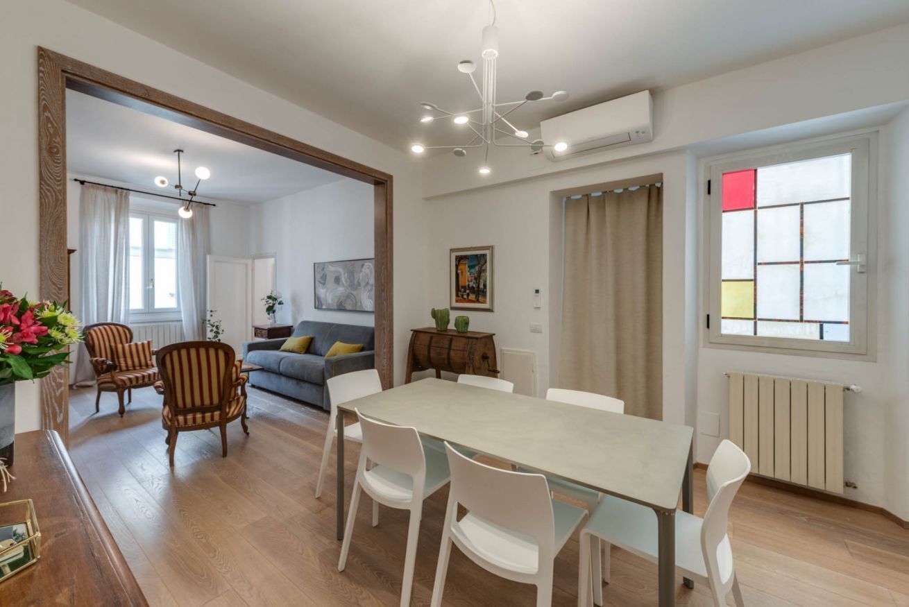 Una sala moderna con comedor, suelo de madera y un amplio ventanal con cortinas.