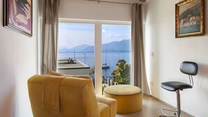 Une pièce avec vue sur un lac et des montagnes, un fauteuil jaune, un pouf rond et une chaise noire.