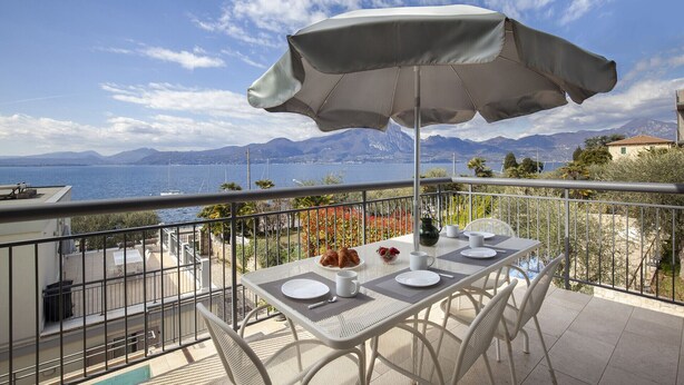 Un balcon avec une table dressée pour deux personnes, un parasol et une vue imprenable sur la mer et les montagnes.