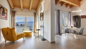 Un salon moderne avec un fauteuil jaune, un coin repas avec des chaises transparentes et une vue sur les montagnes grâce à de grandes fenêtres.