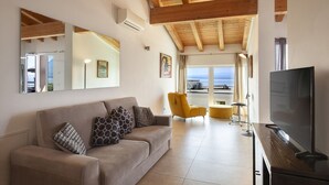 Un salon avec un canapé, un fauteuil jaune, une télévision et une grande fenêtre donnant sur un beau paysage.