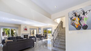 Un amplio espacio de estar con un sofá gris, una mesa de comedor y una escalera que sube a otro nivel.