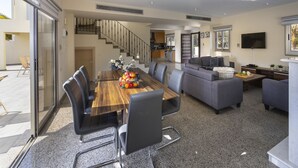 Una sala de estar moderna con una mesa de comedor de madera, sofás grises y una escalera que sube a un nivel superior.