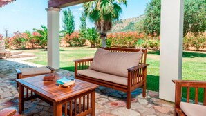 A wooden outdoor seating area with a sofa and tables, surrounded by a stone patio and lush greenery. - CAN CORRÓ - Villa with private pool in Alcudia. Free WiFi (Alcúdia)