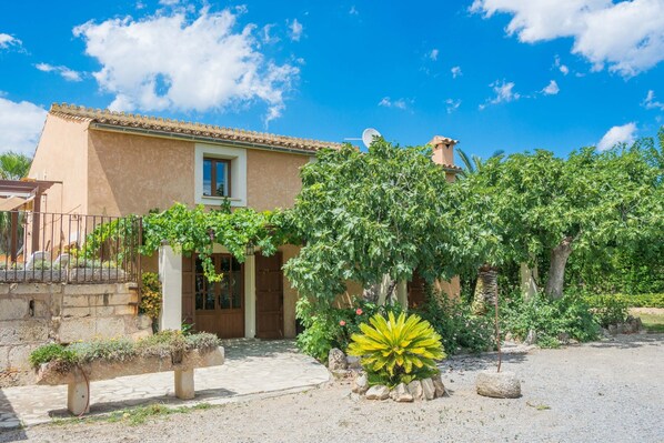 A house with a tiled roof, a front door, and a small window. There is a garden with a bench and a large plant. - CAN CORRÓ - Villa with private pool in Alcudia. Free WiFi (Alcúdia)