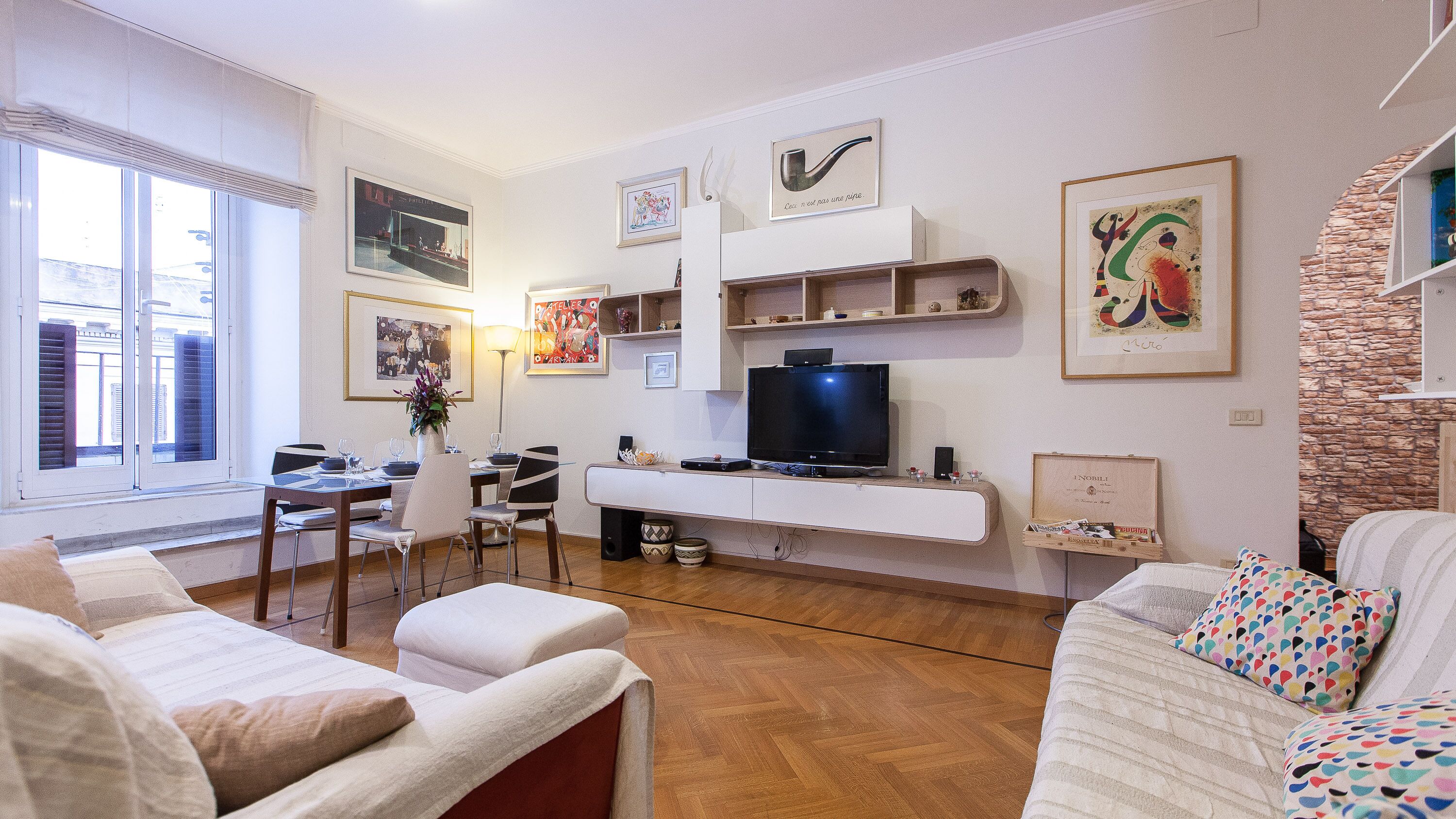 Un salon comprenant un téléviseur, une table à manger, des chaises et des œuvres d’art accrochées aux murs.
