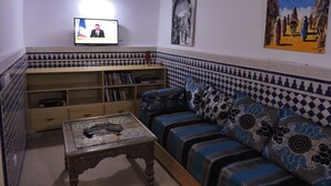 Una sala de estar con un sofá, una mesa de centro, un televisor y una estantería.
