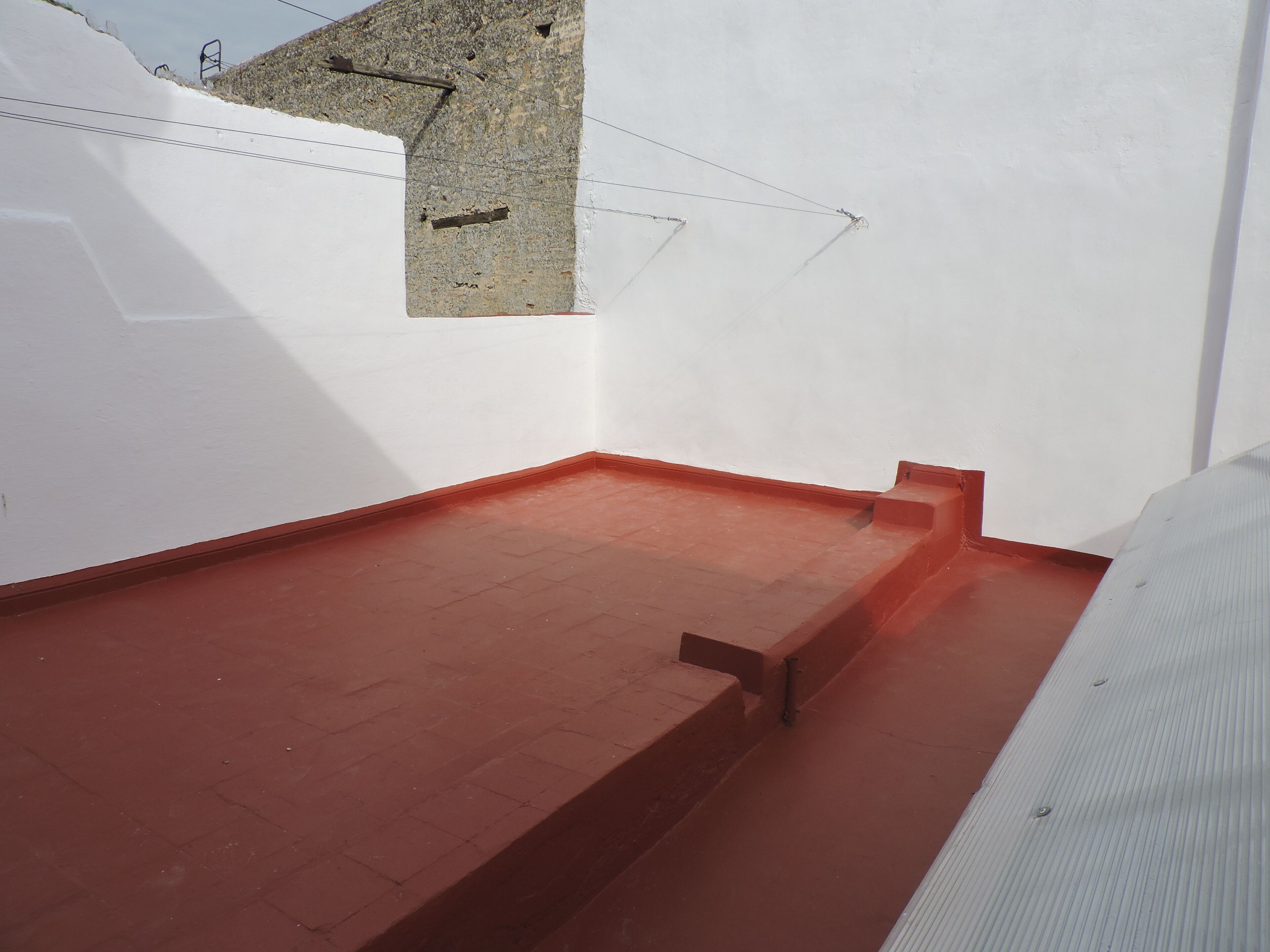 Une pièce avec un sol carrelé de carreaux rouges, un mur blanc et une petite fenêtre.