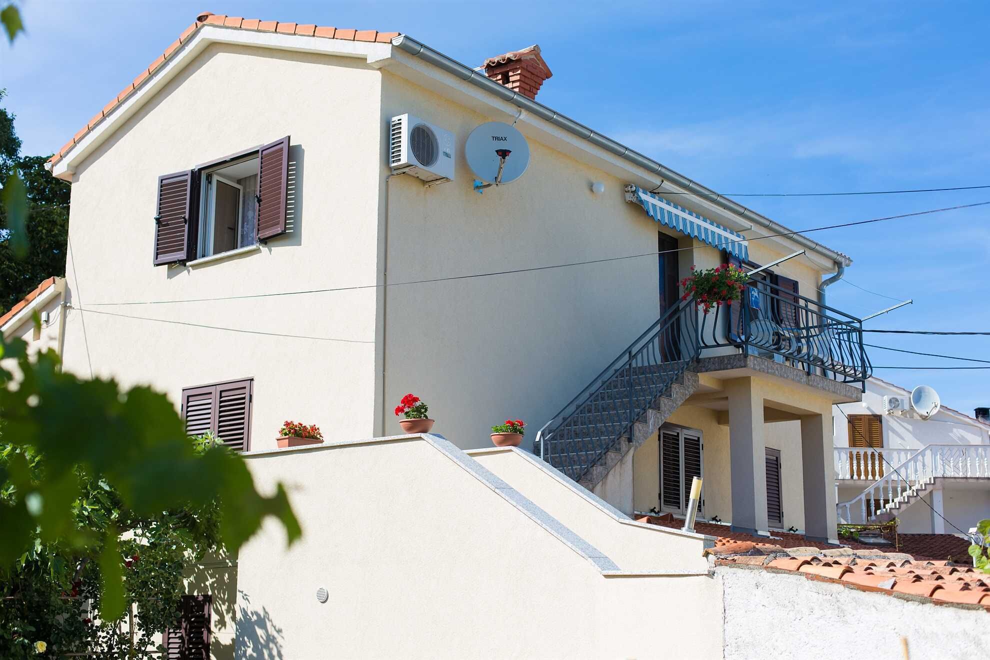 Ein zweistöckiges Gebäude mit einem Balkon, einer Satellitenschüssel und Topfpflanzen.