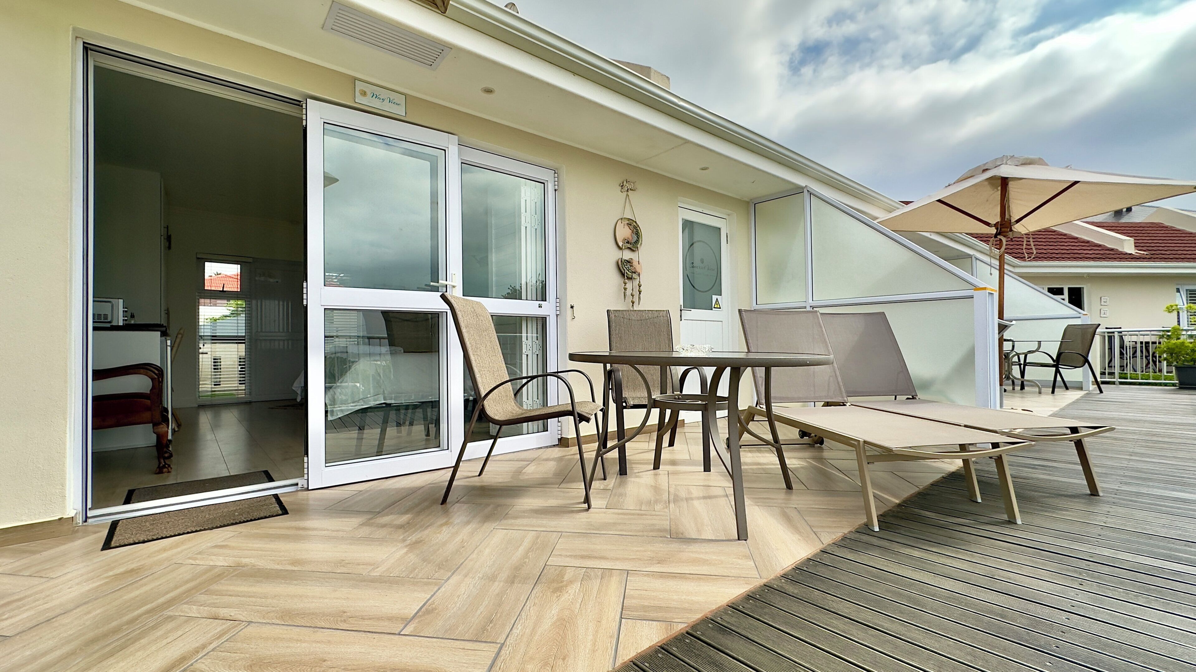 Een overdekte terras met een tafel en stoelen, een schuifpui en uitzicht op de straat.